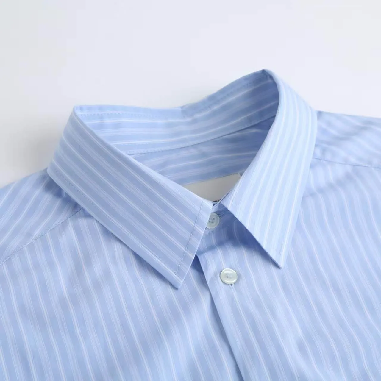 AMI Embroidered Striped Shirt Fabric Selection: Made of 100% cotton poplin fabric. The pure cotton fiber can quickly absorb moisture and perspire, making it refreshing and not stuffy when worn for a long time. The unique plain weave process of poplin makes the fabric both soft and skeletal, not easy to wrinkle and deform, and the upper body is neat and clean. Coupled with the fine blue and white stripes all over the body, the light color scheme is gentle and elegant, which can meet the needs of different scenes. Process 1: Accurately mark the embroidery position on the chest patch pocket to ensure that the pattern does not shift and does not destroy the overall beauty of the striped fabric. High-count embroidery threads of the same color as the fabric are selected, and flat stitch embroidery technology is used. The stitches are evenly tracked, the edges are clean and neat, and the love outline is simple and smooth. It retains recognition without irritating the skin. It is blended into the striped texture in a low-key manner to avoid an abrupt feeling, while ensuring that the embroidery threads are Wear-Resistant. 2: After the embroidery is completed, perform high-temperature ironing and thread trimming to ensure that the pattern is smooth and compliant, and it is not easy to lose thread or warp after being worn for a long time. Details: 1. The collar seat adopts double-layer reinforcement technology, which is not easy to collapse and deform after long-term wear. The collar corner has a soft arc, which can modify the neck line without being too sharp, making it neat and decent. 2. The inner side of the placket has hidden hemming treatment to avoid burrs on the fabric, while enhancing structural stability and preventing it from deforming after multiple washes. Accessories: One-to-one customized buttons Size: S M L XL Style number: D 236